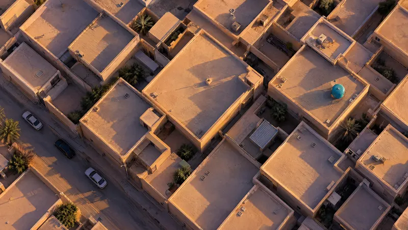 منظر جوي لأسطح مستوية بلون الرمل في حي سعودي وقت الغروب، وعلى أحدها خزان ماء سماوي اللون.